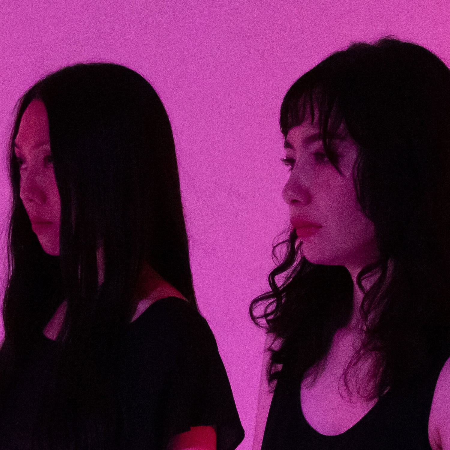 Two woman looking away from camera in pink lighting.