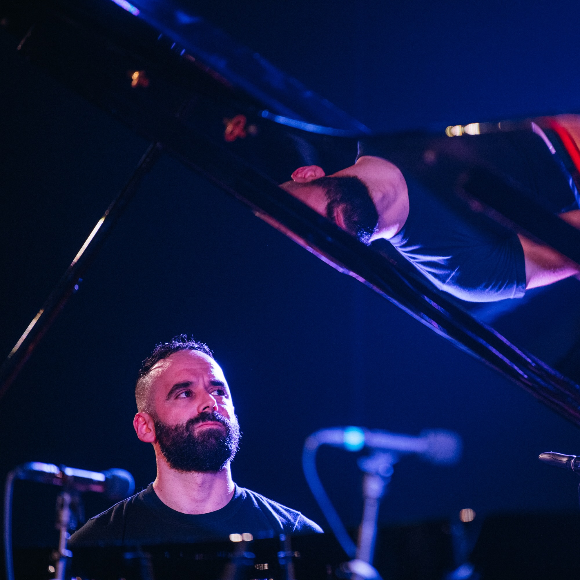 Adam Tendler sitting at the piano looking up toward the open lid.