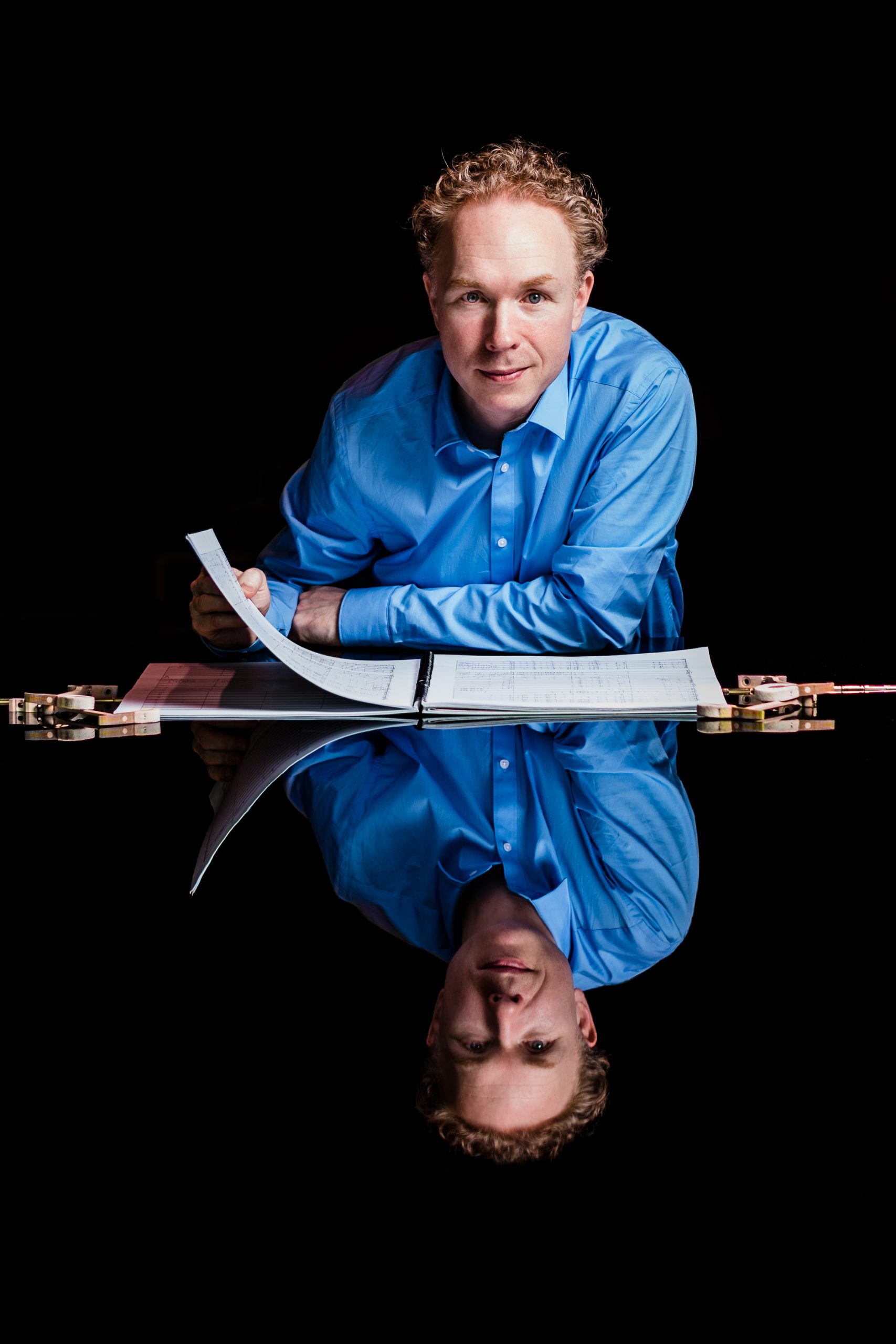 Ralph van Raat leaning on a piano with a large, bound score